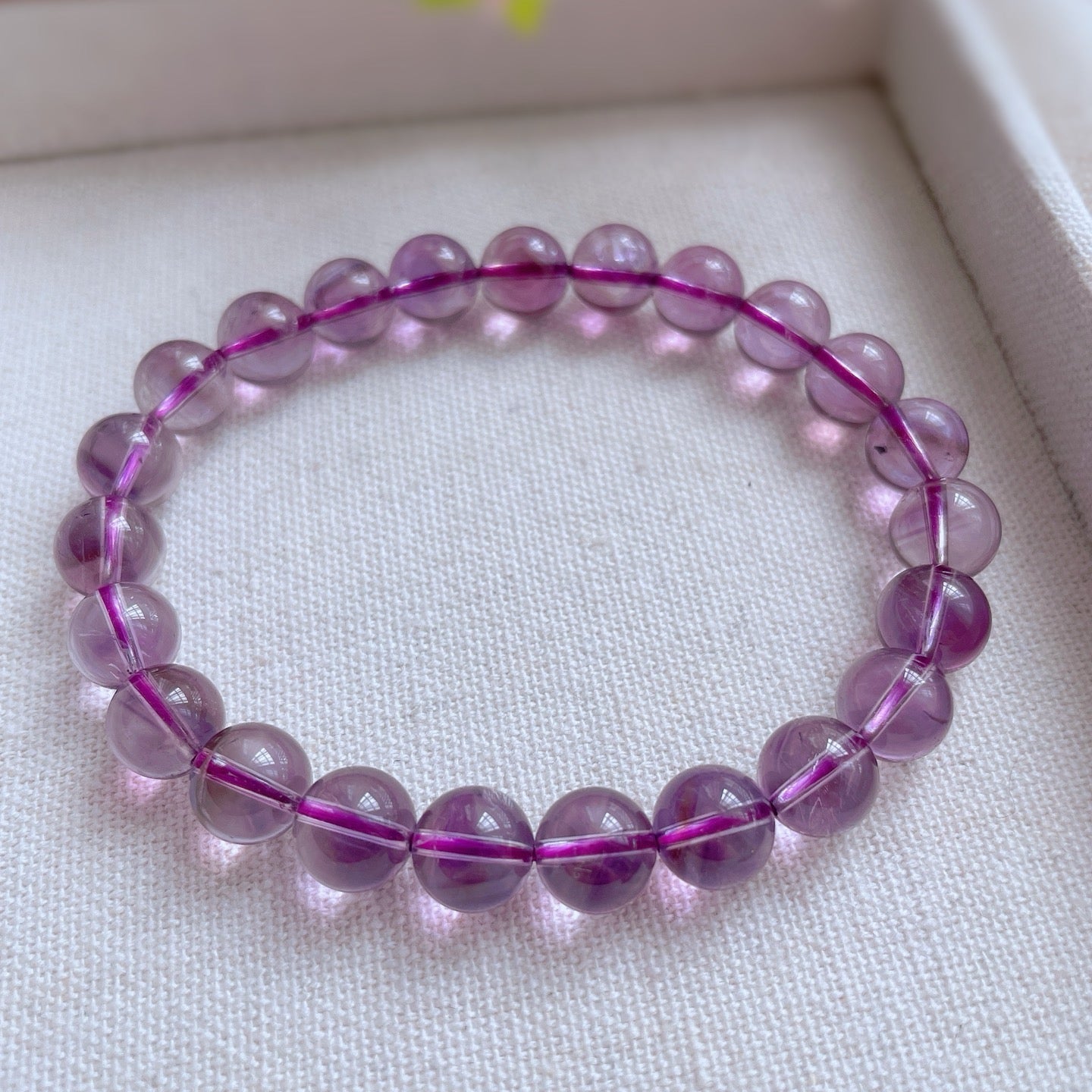 Purple beaded bracelet on a light pink surface with blurred floral background